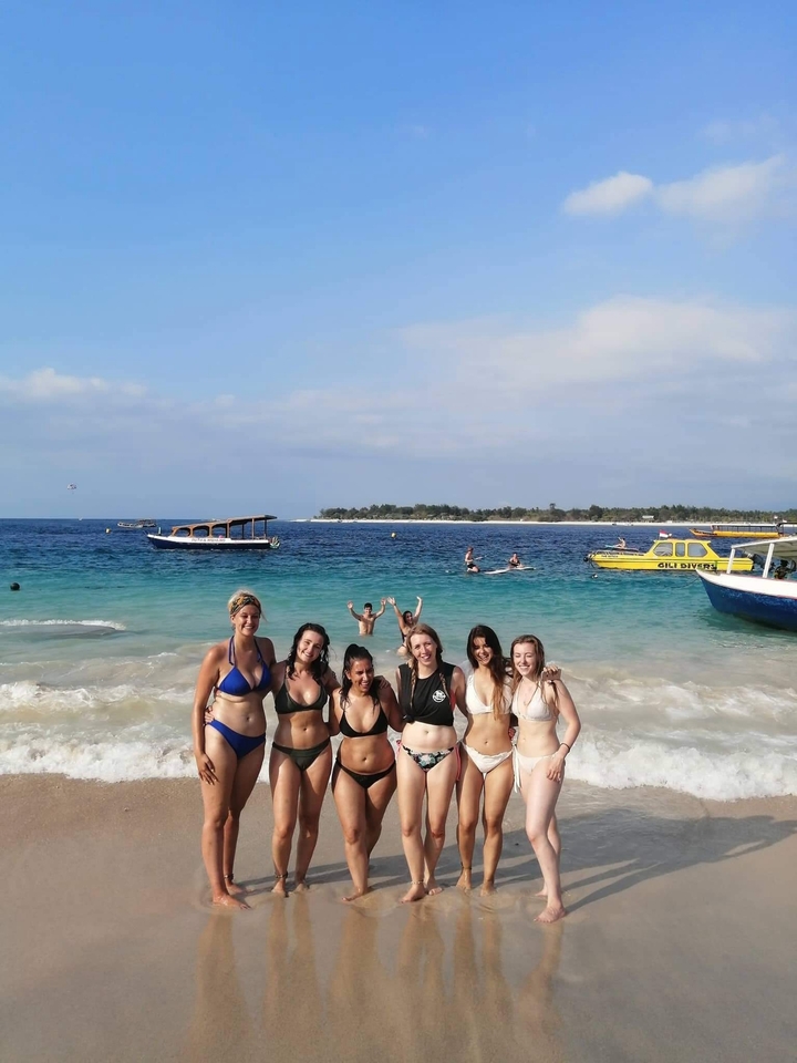 Group of people posing at the beach with boats in the background.