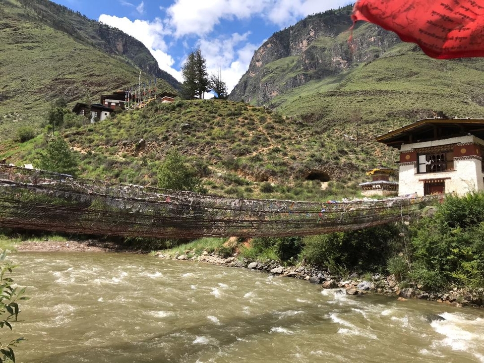 Suspension bridge over a river with hills in the background.