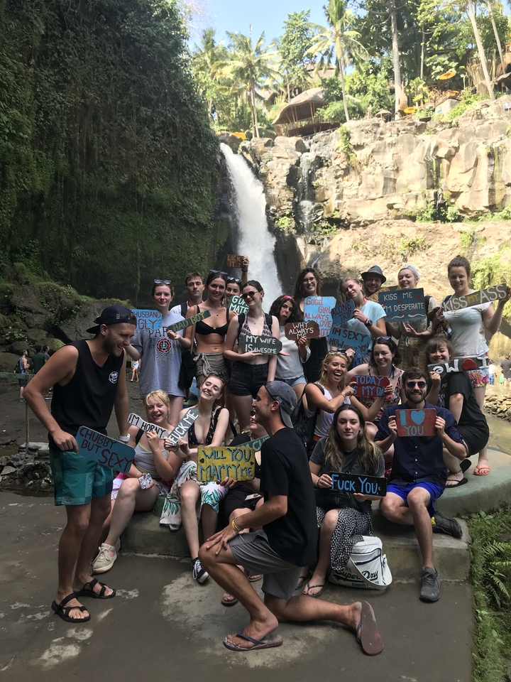 Group of people posing in front of a waterfall holding signs.