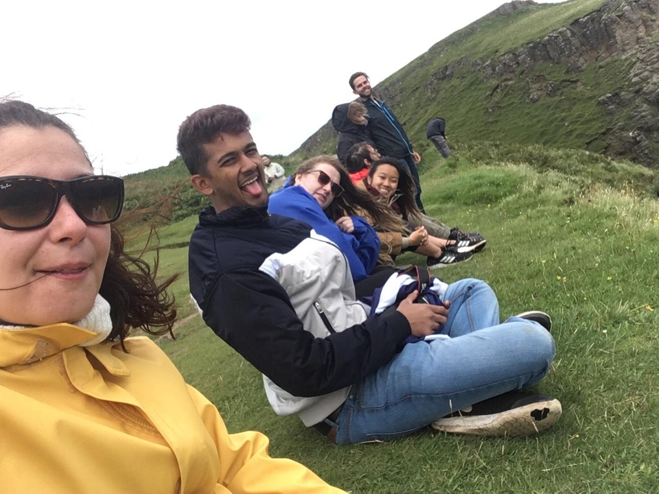 Group of people sitting on a grassy hill, some making funny faces.