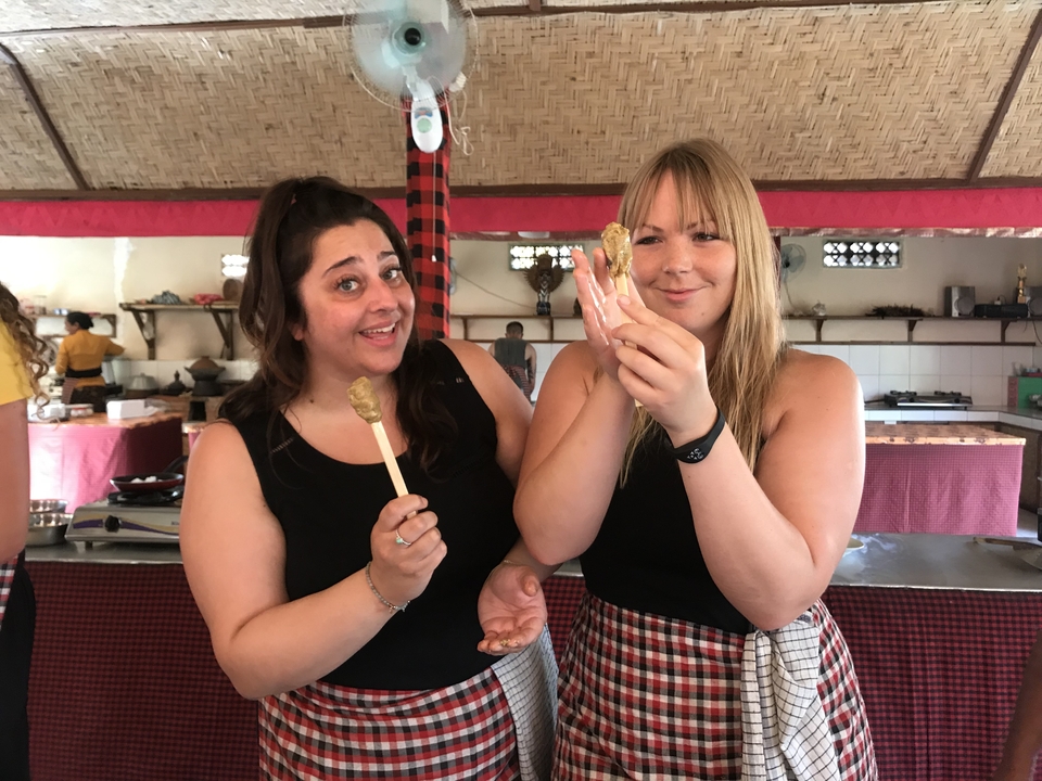 Two women smiling and holding food on sticks.