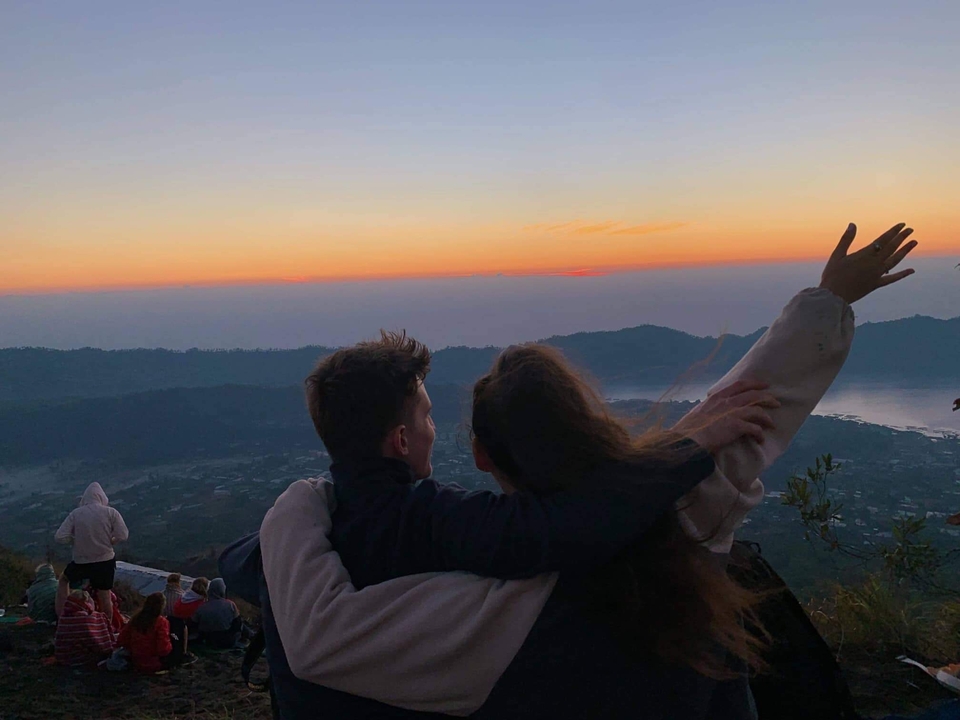 Two people embracing, enjoying a sunset view over a landscape.