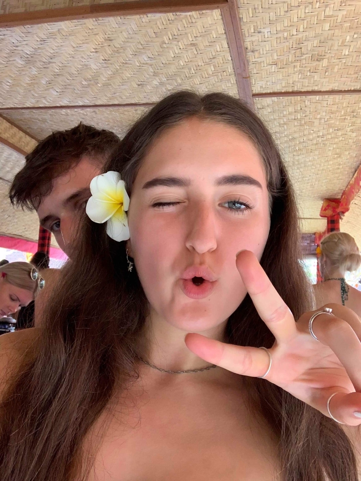 A close-up of a winking person with a flower in their hair.