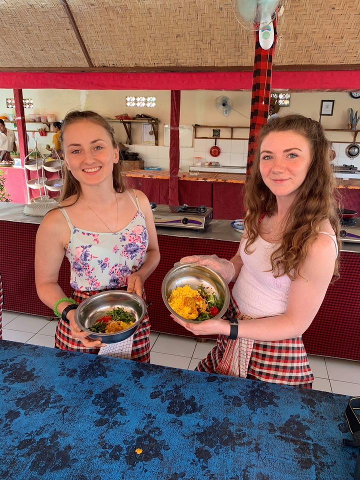 Two women holding dishes with food in a cooking class.