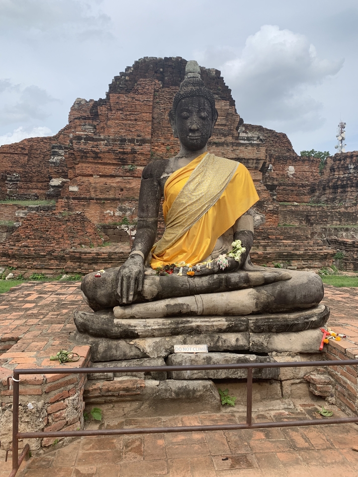 Large stone Buddha statue with flowers on a lap.