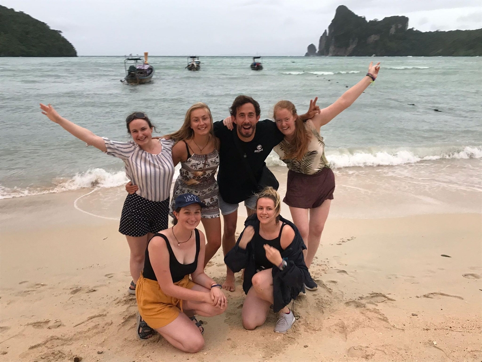 Group of people posing on a beach with boats in the background.