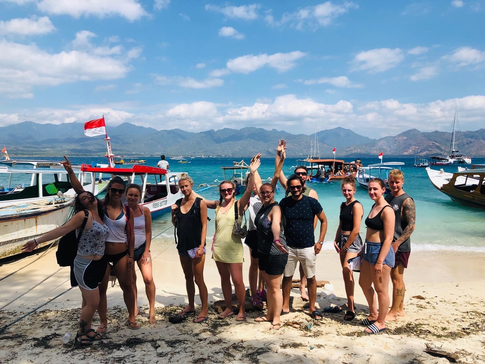 Group photo of people on a beach with boats and water in the background.