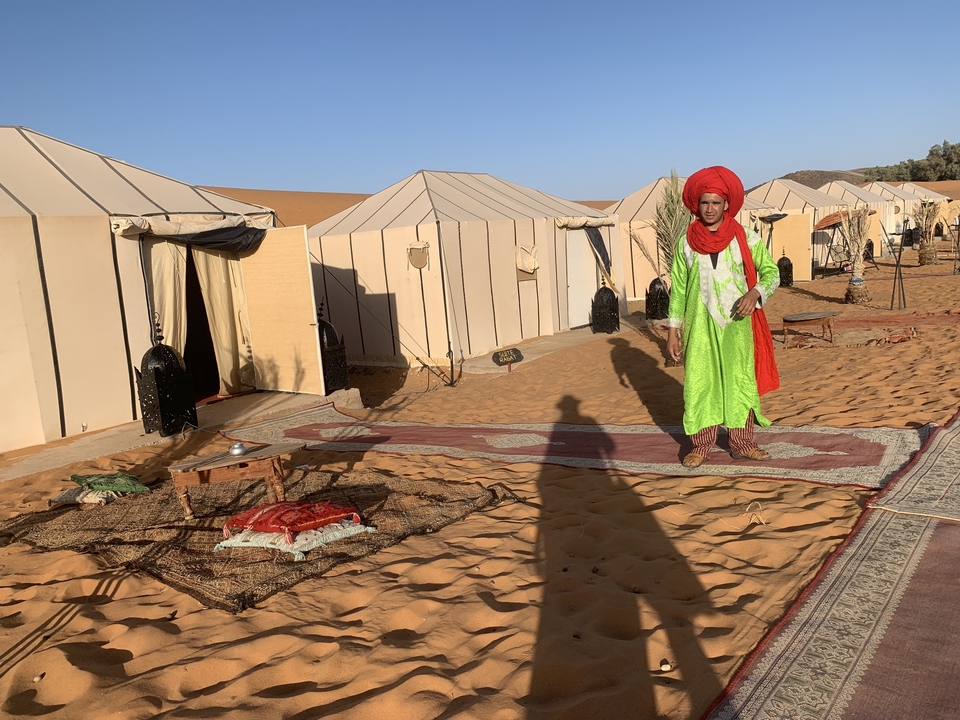 Personne en tenue traditionnelle debout à l'extérieur de tentes dans un désert.