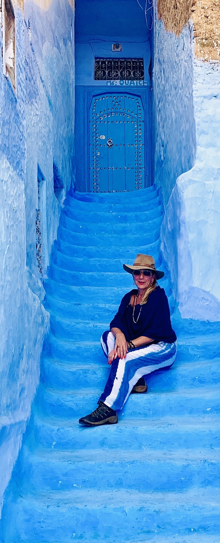Femme avec un chapeau assise sur des marches bleues.
