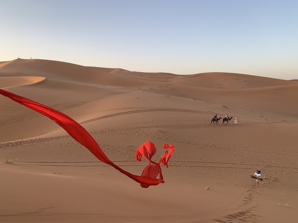 Paysage désertique avec chameaux et tissu rouge flottant.