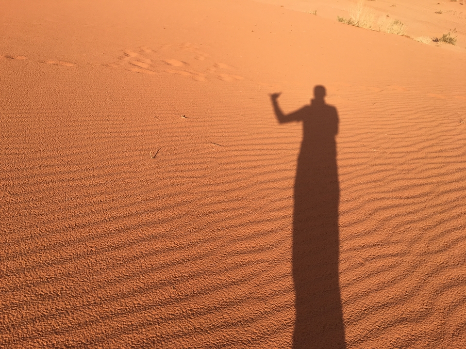 L'ombre d'une personne faisant un geste de la main sur des dunes de sable orange.