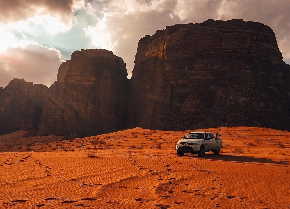 Véhicule tout-terrain garé sur le sable avec des falaises imposantes en arrière-plan.