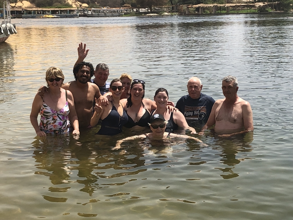 Groupe de personnes debout dans l'eau, toutes souriantes et faisant signe de la main.