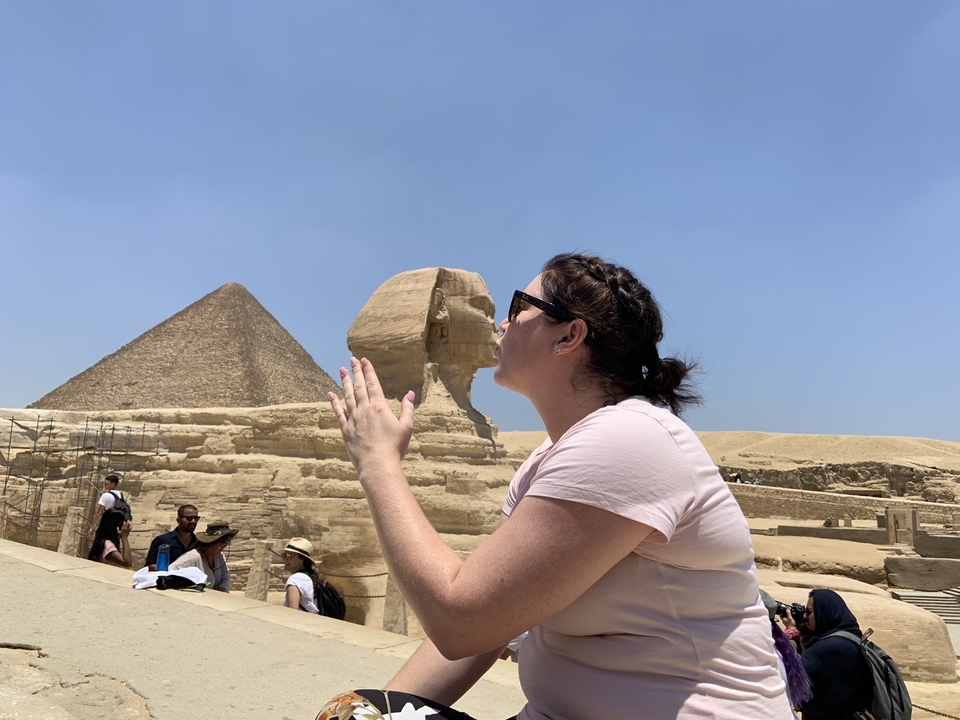 Femme posant devant le Sphinx et la Pyramide avec un geste humoristique.