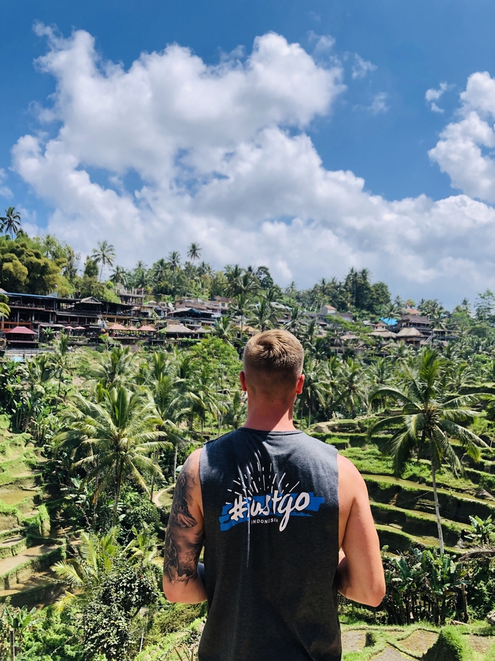 Man looking at terraced hills and buildings with palm trees.