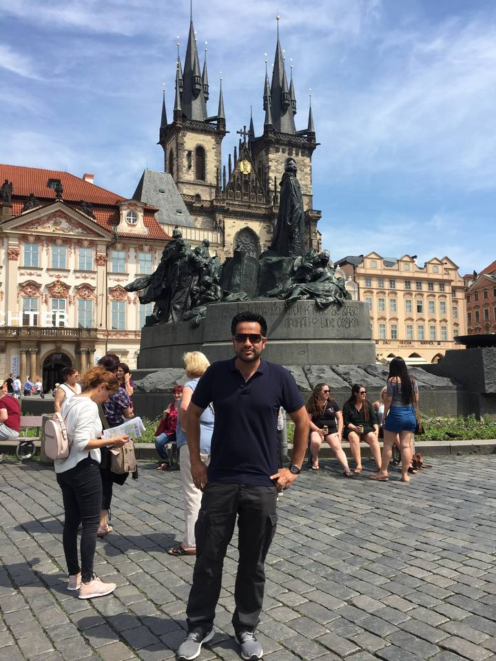Person posing in a busy square with historical statues.