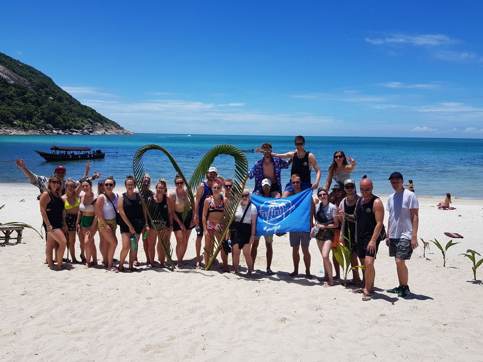 Group photo on a beach with decorative palm leaves.