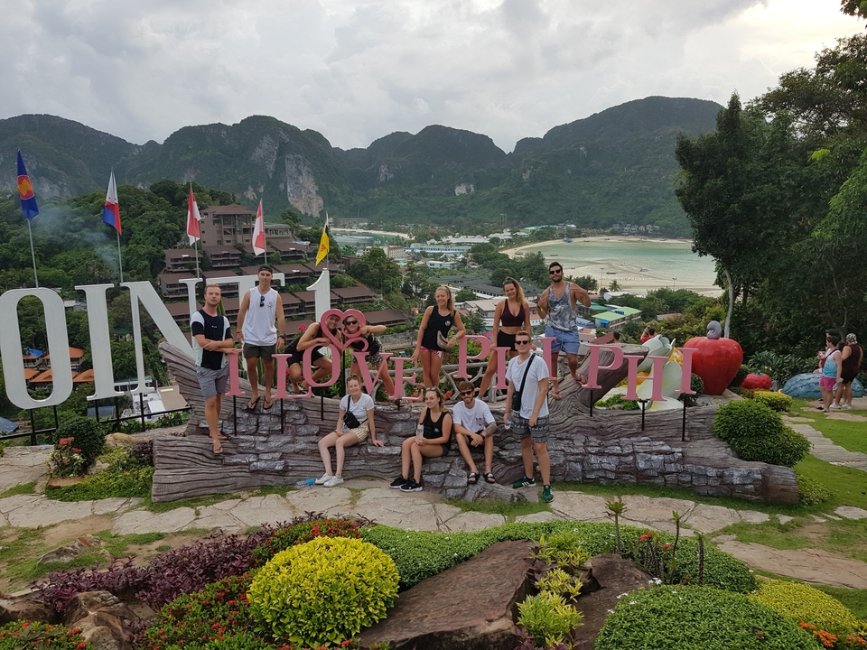 Group in front of 'I Love Phi Phi' sign with beach and mountains.