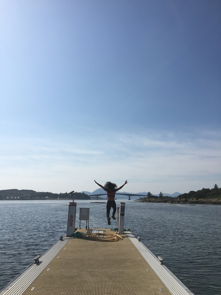 Person with arms raised by water and mountains.