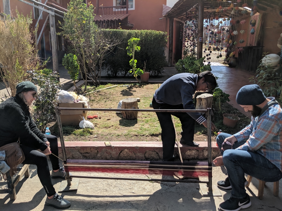 Des gens tissant des fibres à l'extérieur avec un métier à tisser.