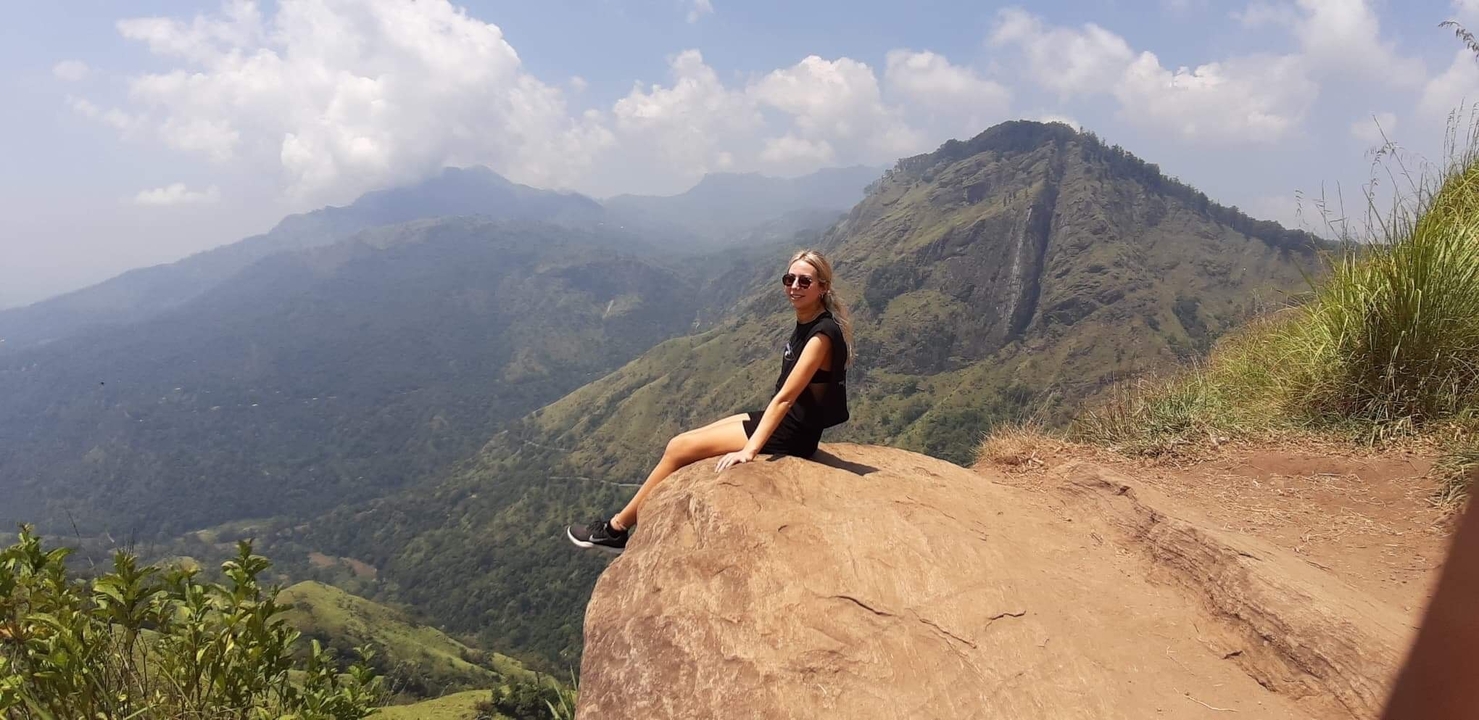 Person sitting on a rock with a scenic mountain backdrop.