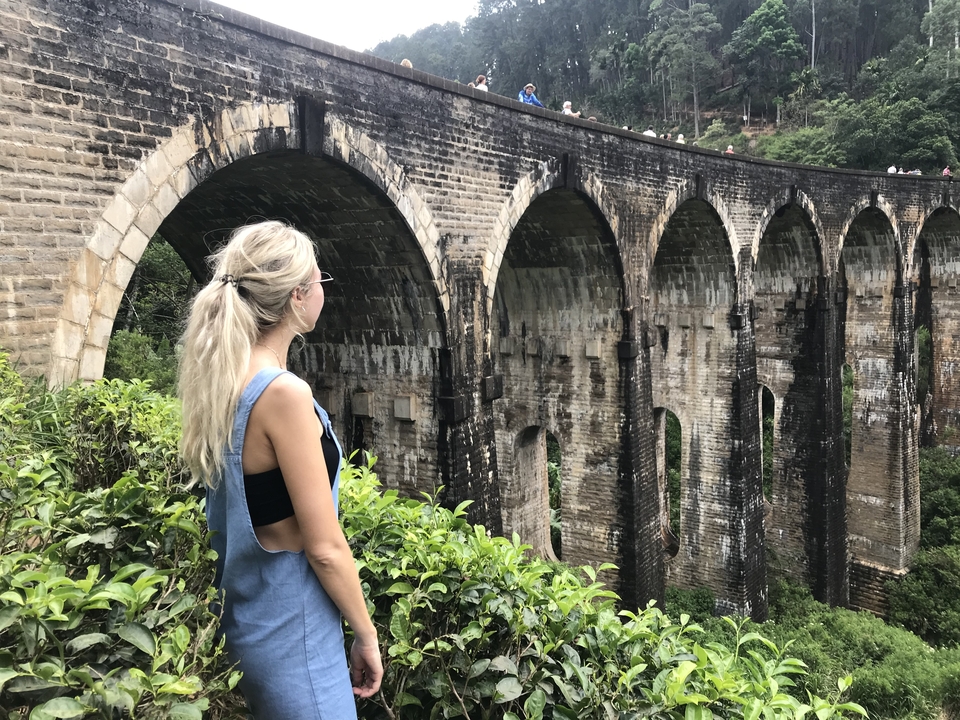 Woman standing beside a large stone bridge with multiple arches.