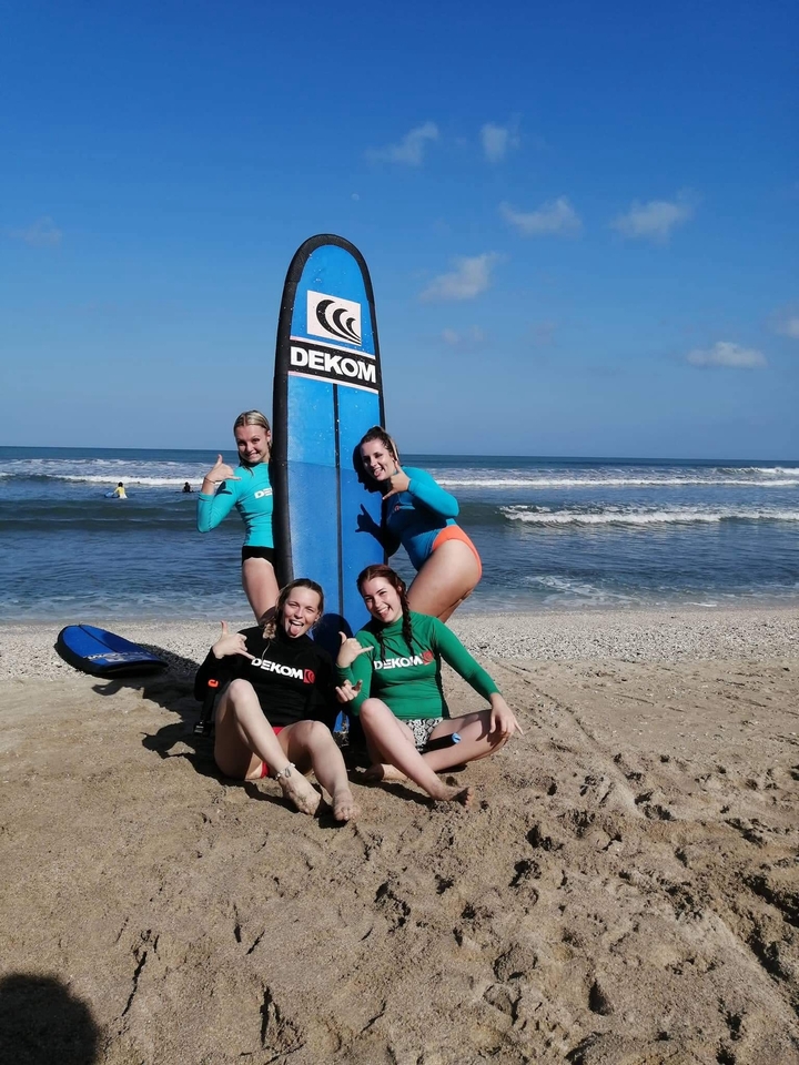 Four people posing with surfboards on a beach.
