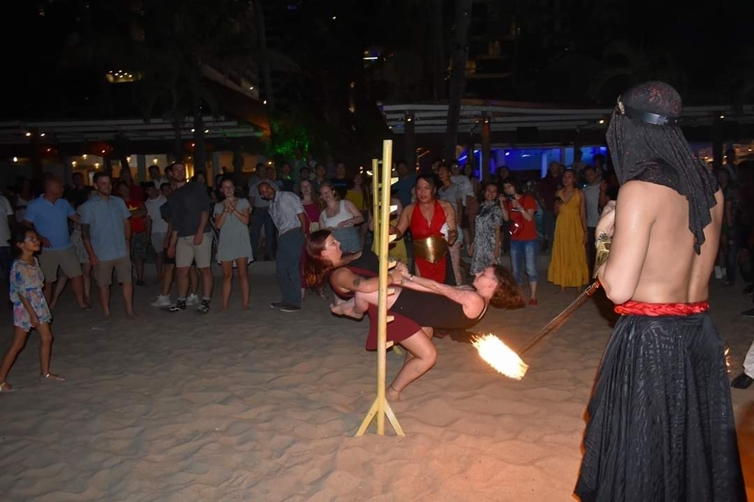 Beach party with people dancing and limbo, a performer holding a flaming stick.