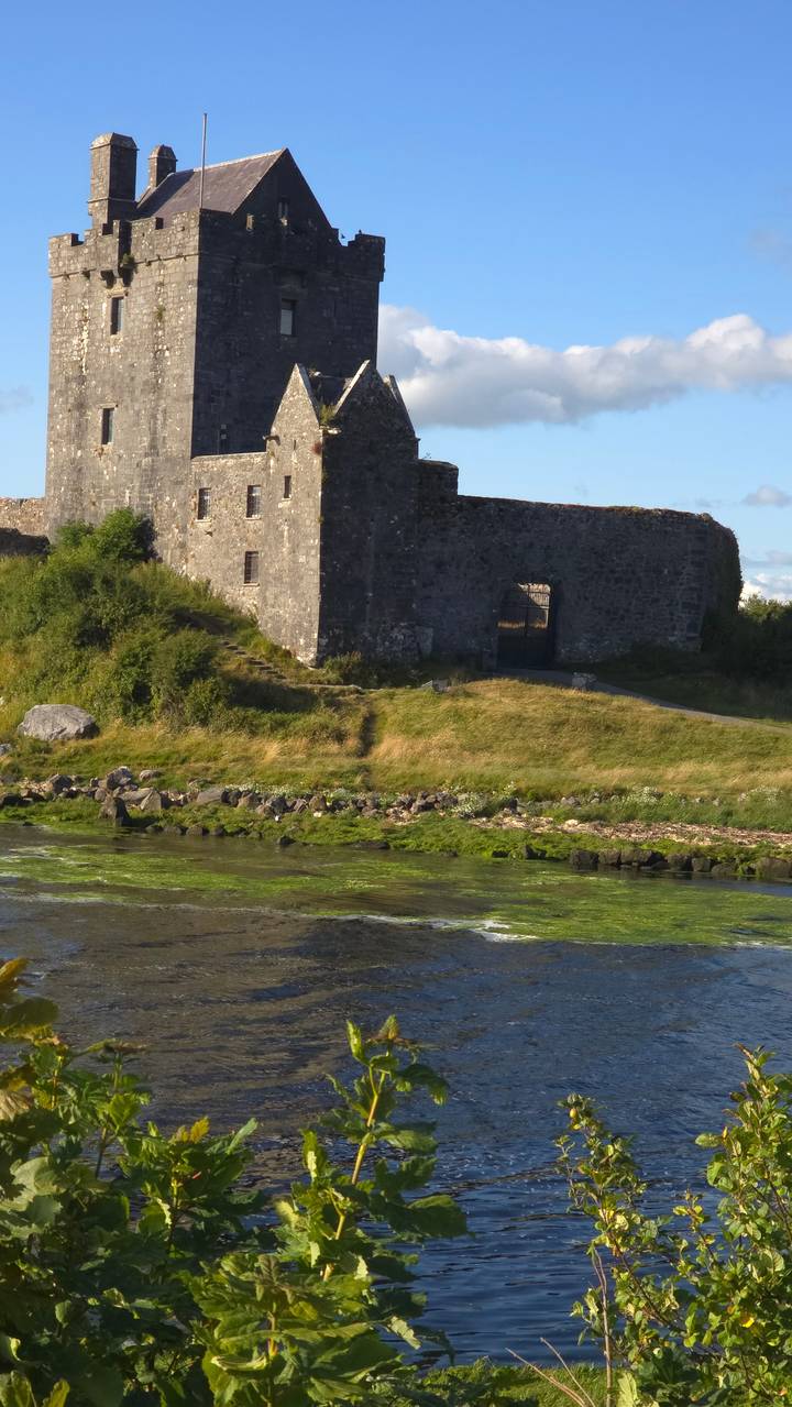 Stone castle by a river under a clear sky.