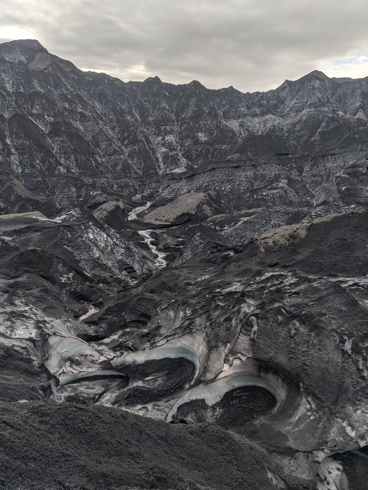 Rugged terrain with volcanic features and a small stream.