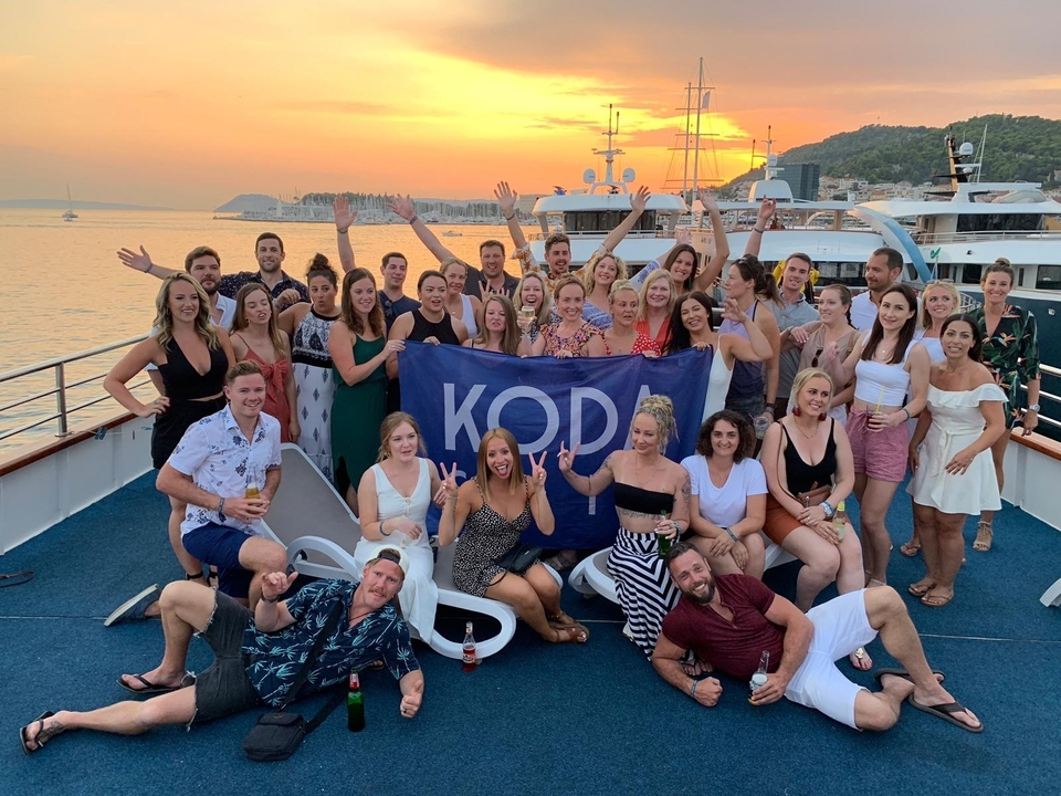 Grand groupe en train de célébrer sur un bateau au coucher du soleil avec une banderole.