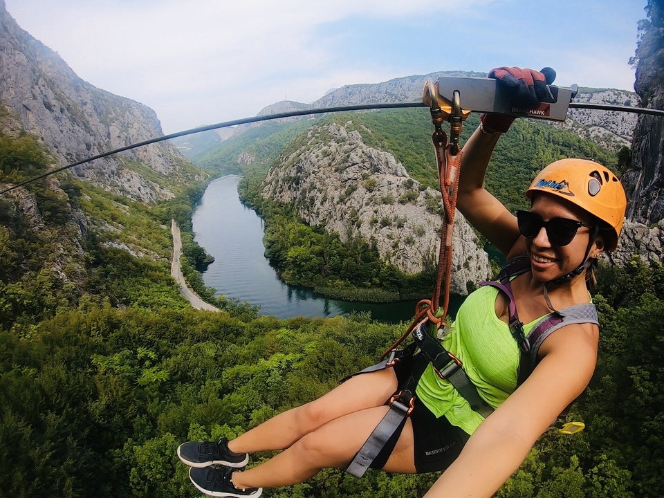 Personne faisant de la tyrolienne au-dessus d'une rivière pittoresque et d'un paysage rocheux.