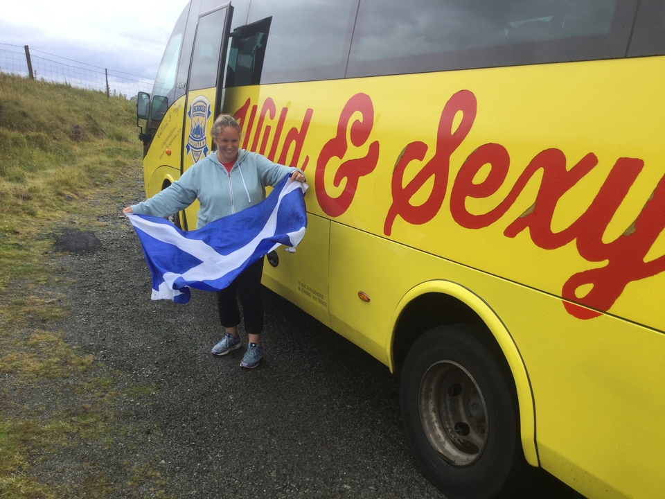 Personne avec un drapeau écossais à côté d'un bus touristique jaune.