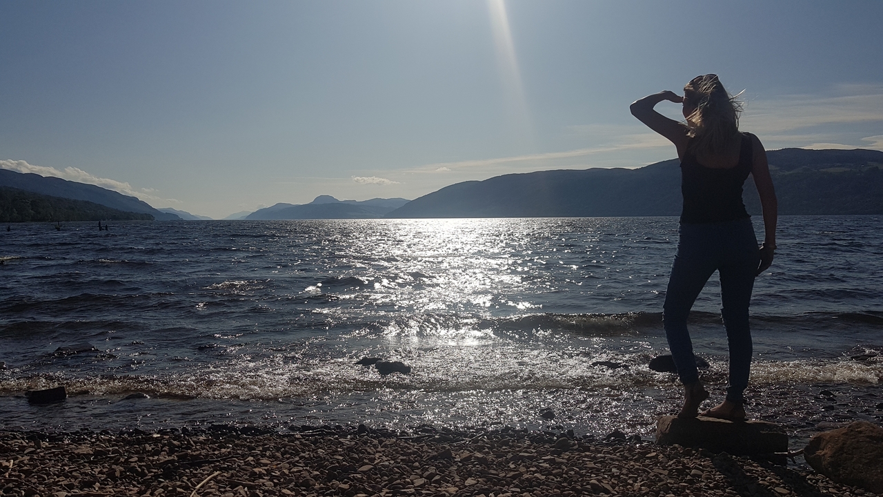 Woman by a lakeside looking into the distance with sun above.