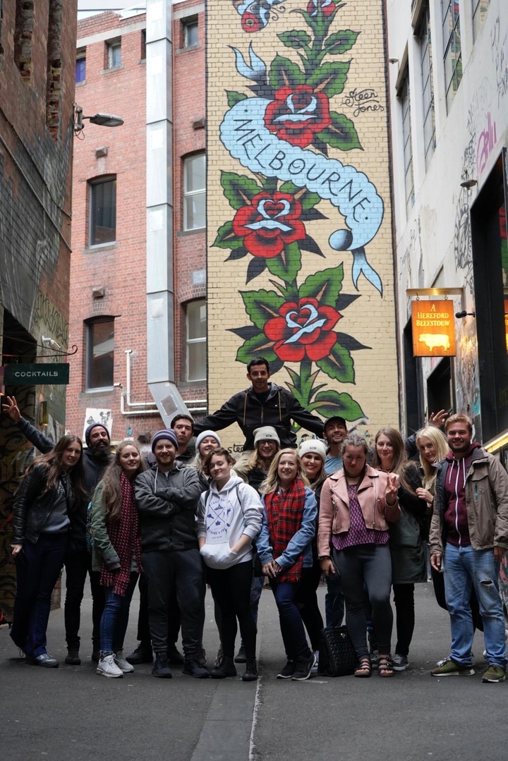 Un groupe de personnes posant devant une fresque dans un environnement urbain.