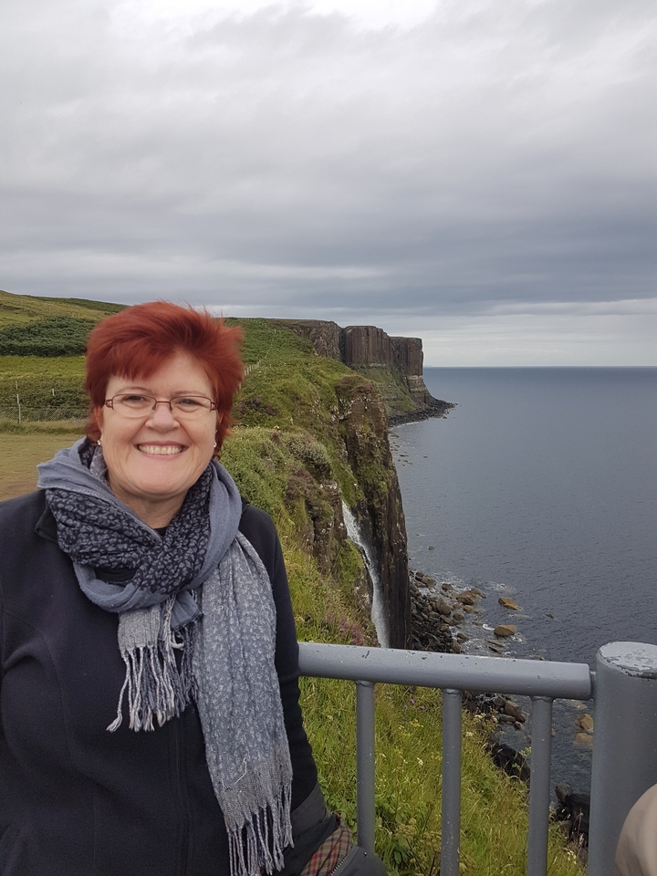 A person smiling with a scenic cliff and sea in the background.