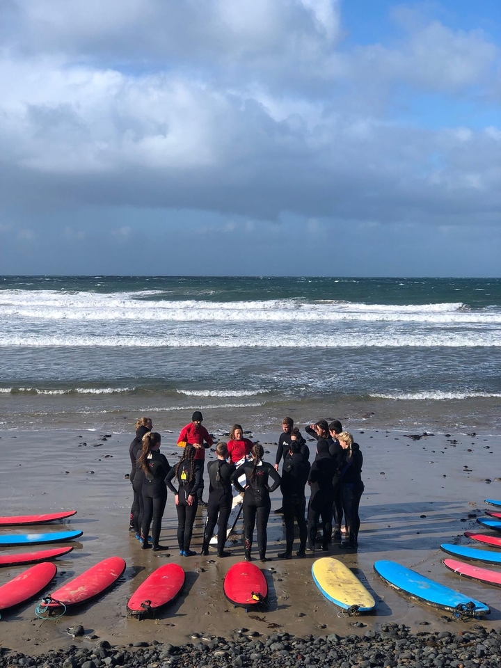 Groupe d'individus en combinaisons de plongée sur une plage venteuse.