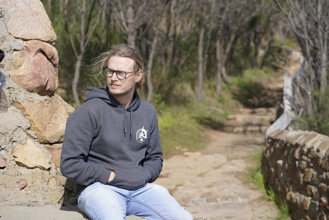 Individu assis sur une structure en pierre dans un cadre naturel.