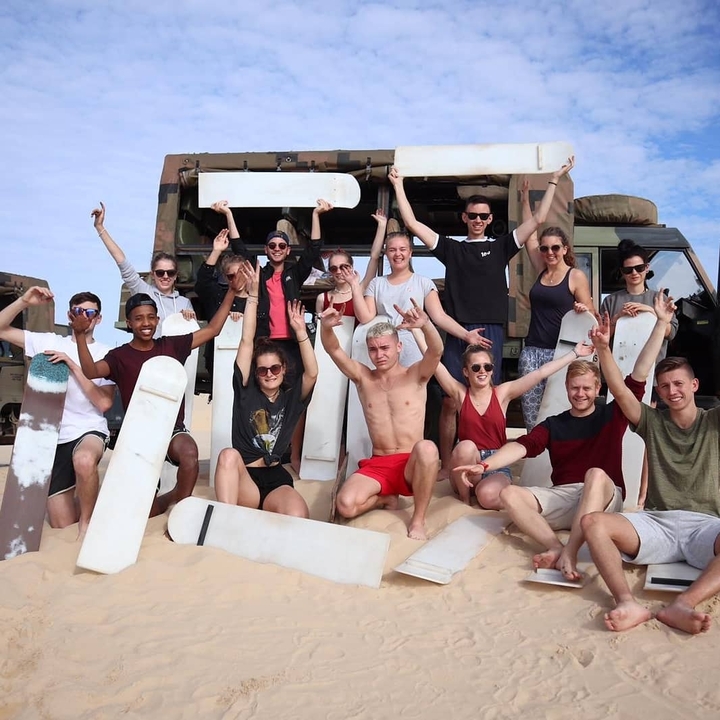 Group of people posing with sandboards on a beach.