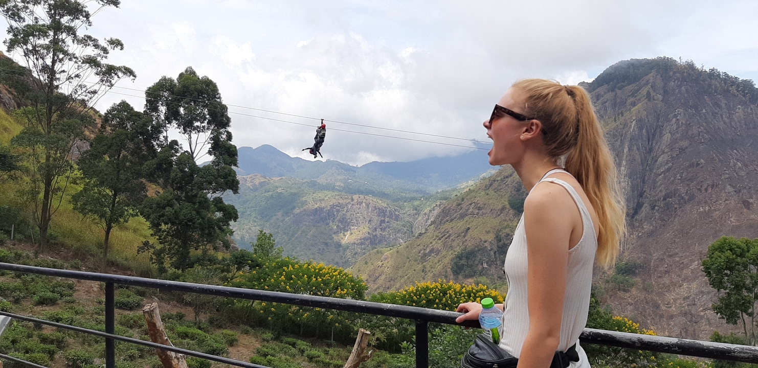 Woman posing with a person ziplining in a scenic mountain area.
