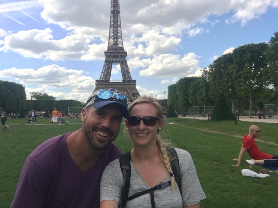 Couple posing in front of the Eiffel Tower on a sunny day.
