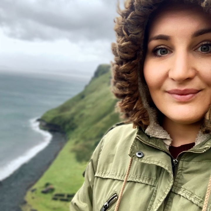 Close-up of a person with a coastal cliff and ocean in the background.