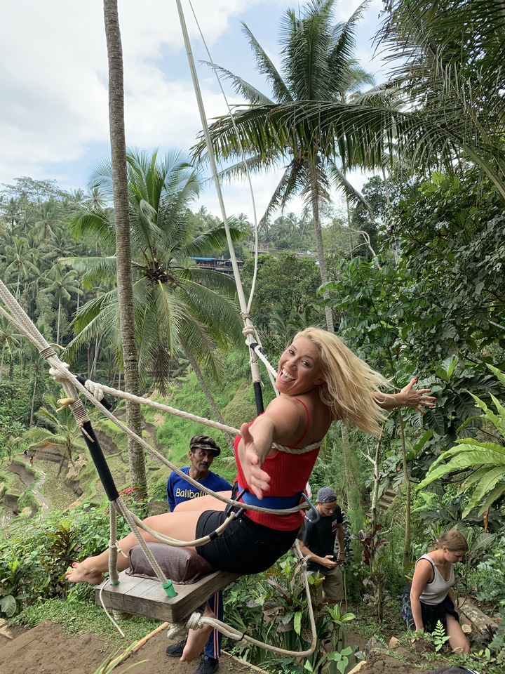 Smiling person on a swing surrounded by lush greenery.