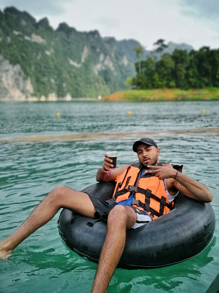 Person floating in a tube on a lake with a drink, set in lush surroundings.