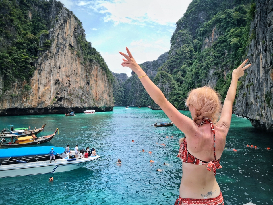 Woman with arms raised on a boat in a tropical bay with limestone cliffs.