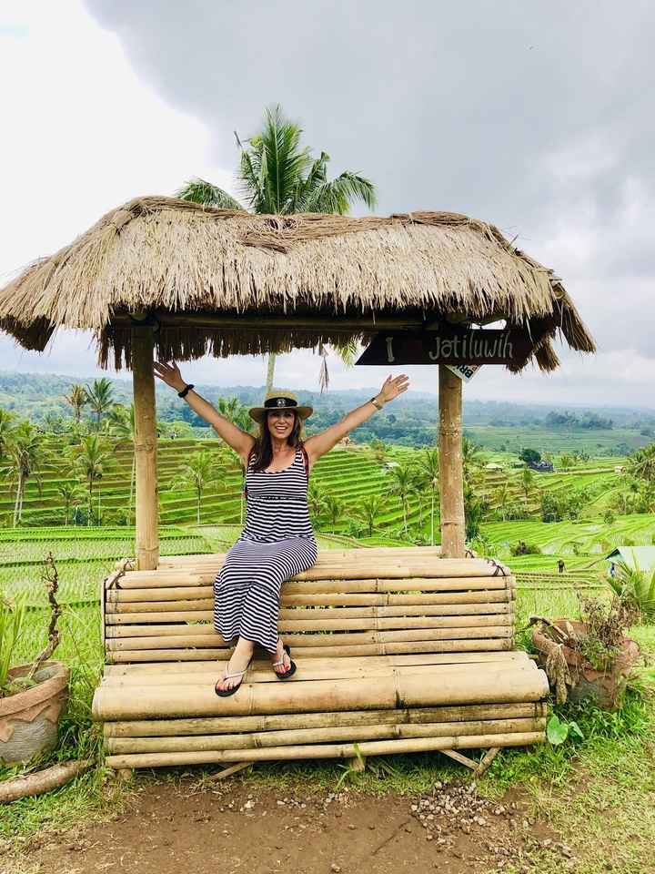 Femme aux bras levés assise sur une structure en bambou dans une rizière en terrasses