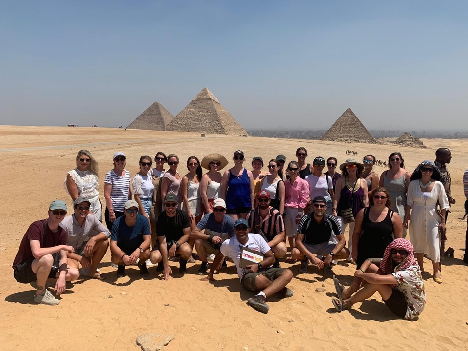 Tourists posing in front of the pyramids in the desert.