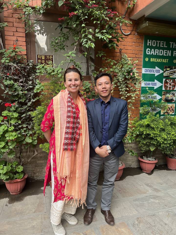 Two individuals posing in traditional attire in front of a building.