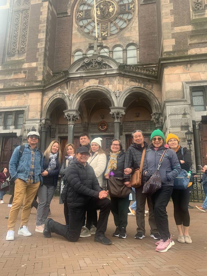 A group of people posing in front of a historical building with a clock.