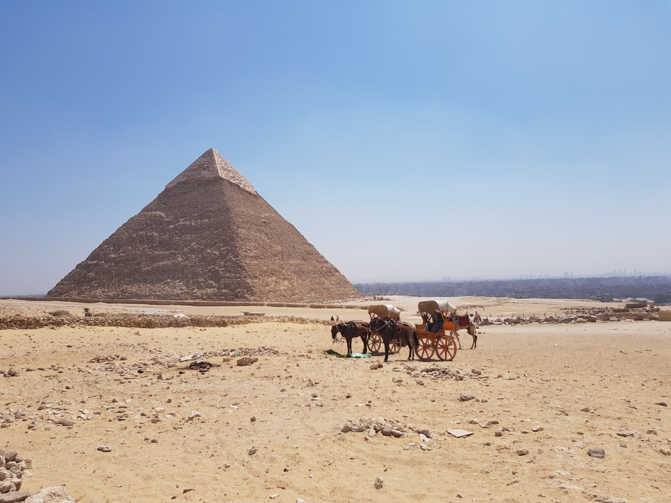 Vue d'une pyramide avec chameau et calèche dans le désert.
